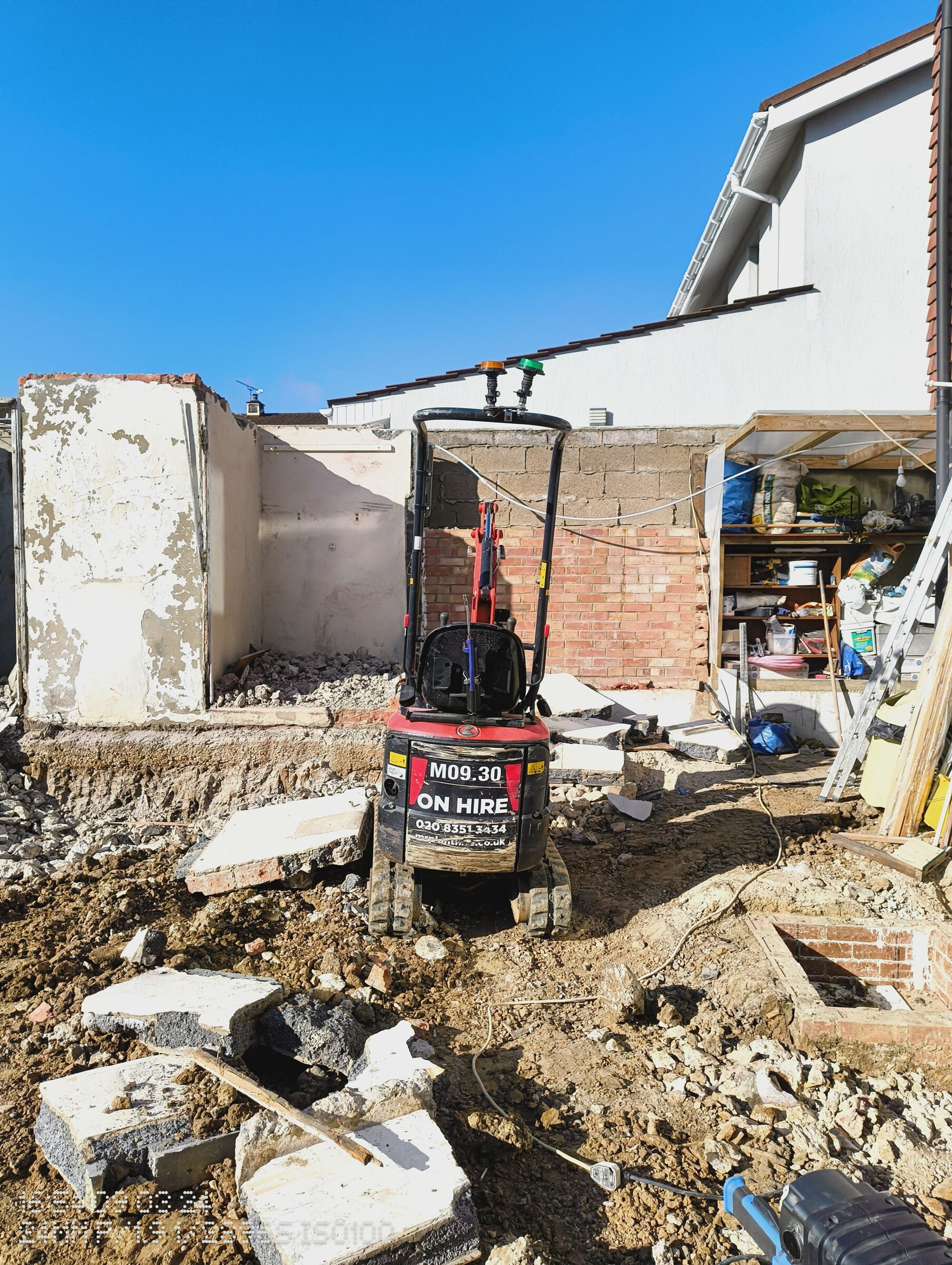 Mini digger standing among broken concrete slabs after the rear structures were taken down.