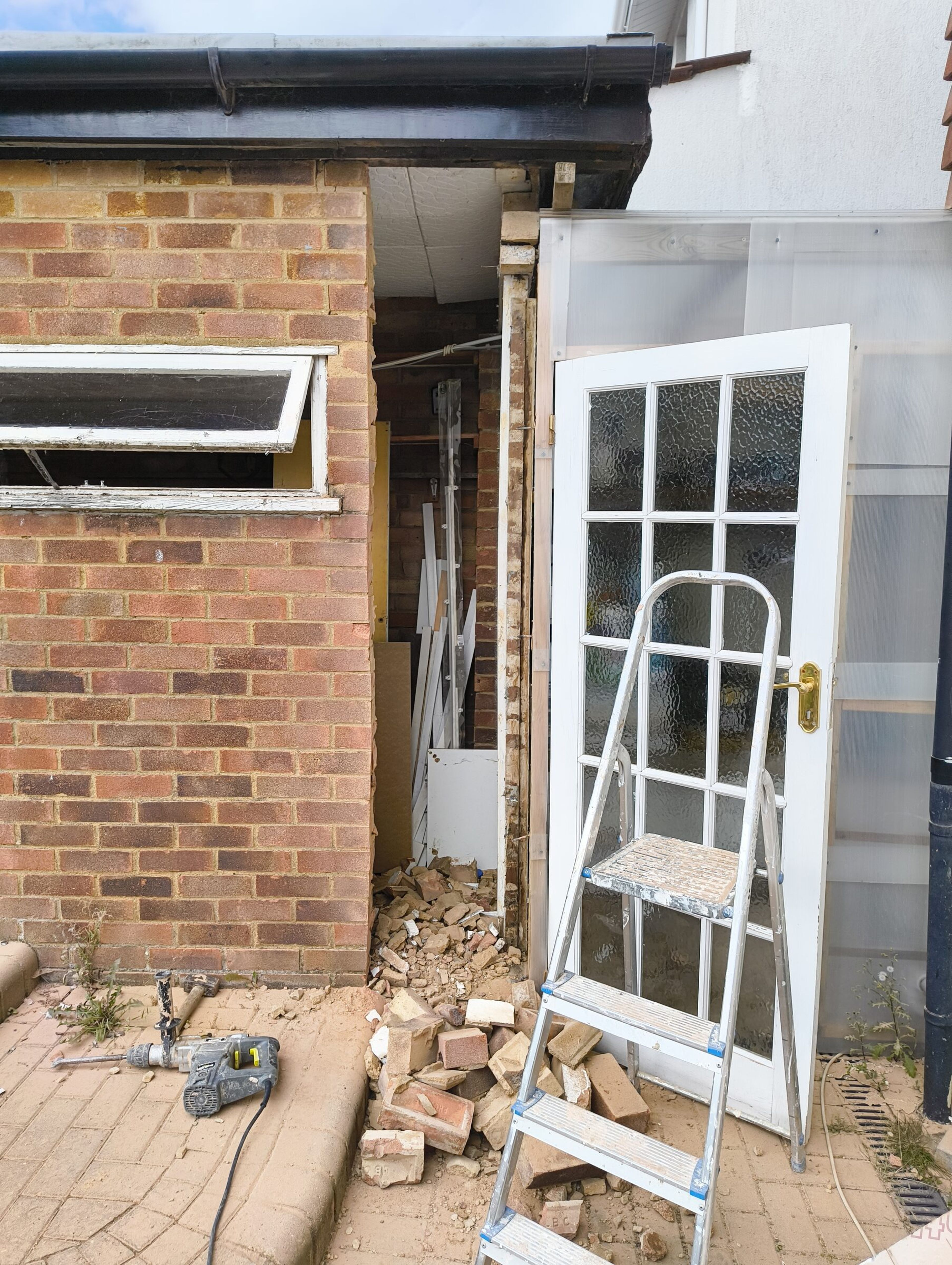 Rubble from the broken opening piled on the patio, with a drill, stepladder, and the glazed door still in place.