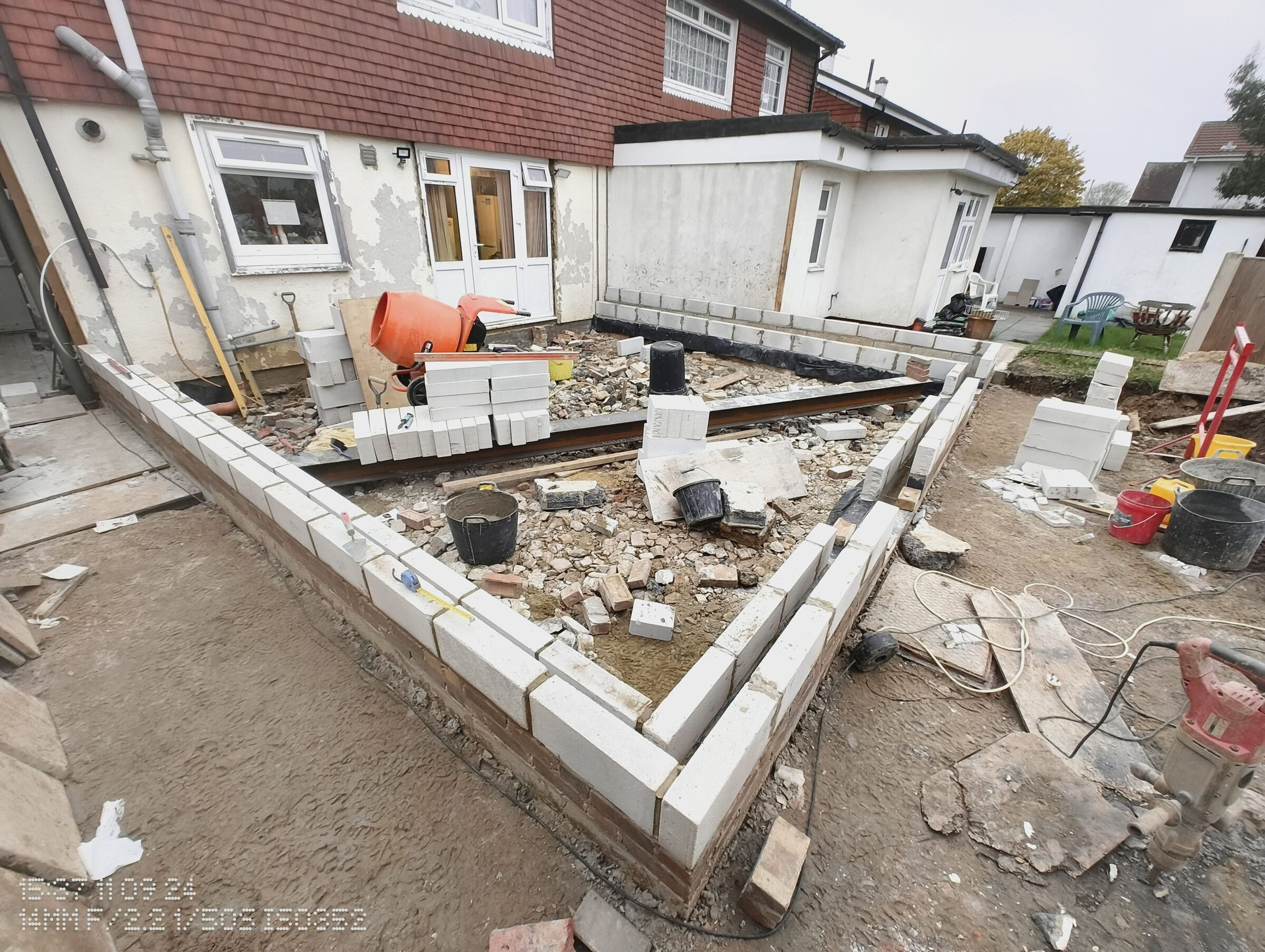 Blockwork walls around the Chigwell rear extension, with the cement mixer and stacks of blocks inside the footprint.