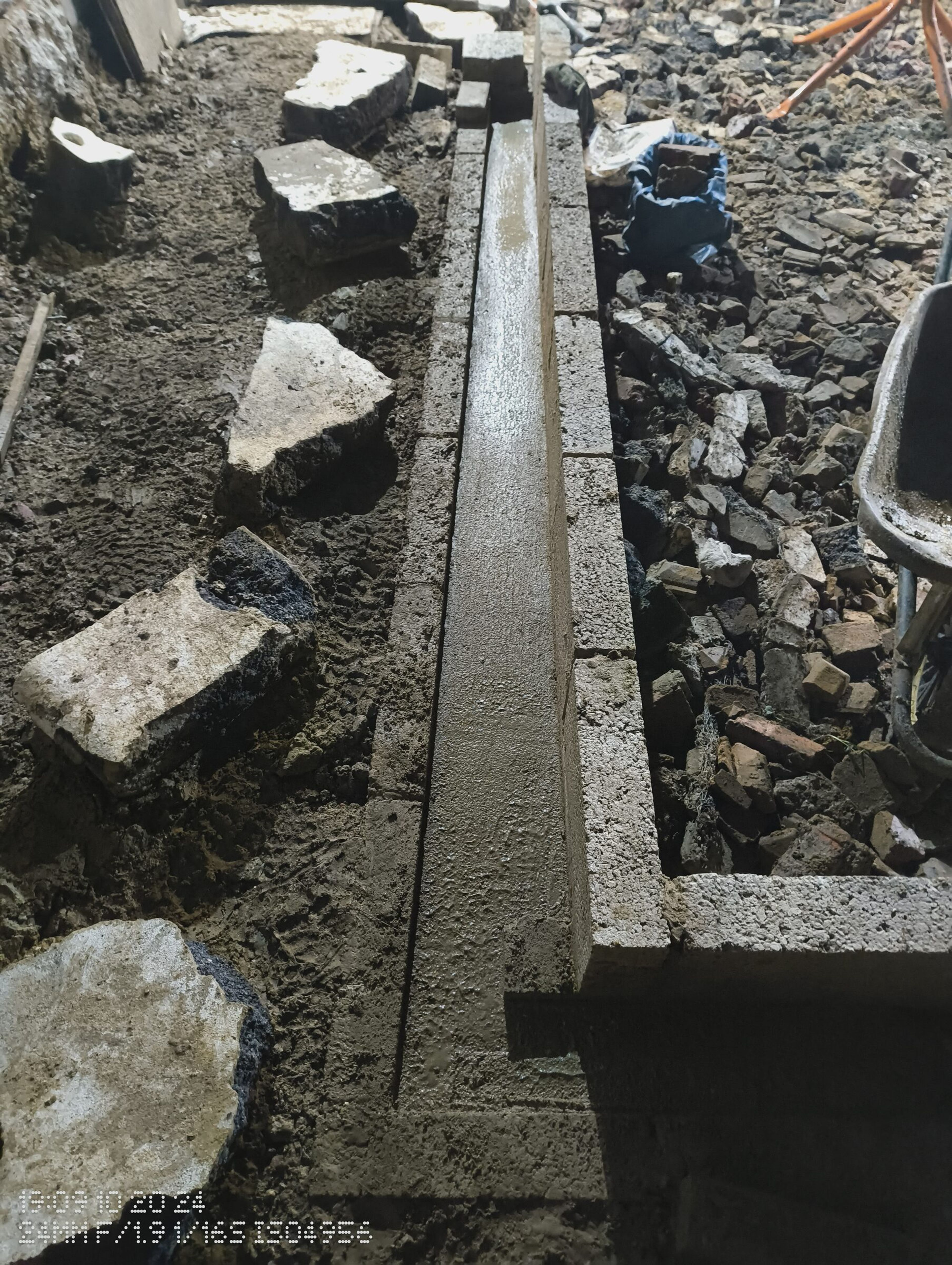 Fresh concrete poured along the foot of the blockwork wall, beside the hardcore fill.