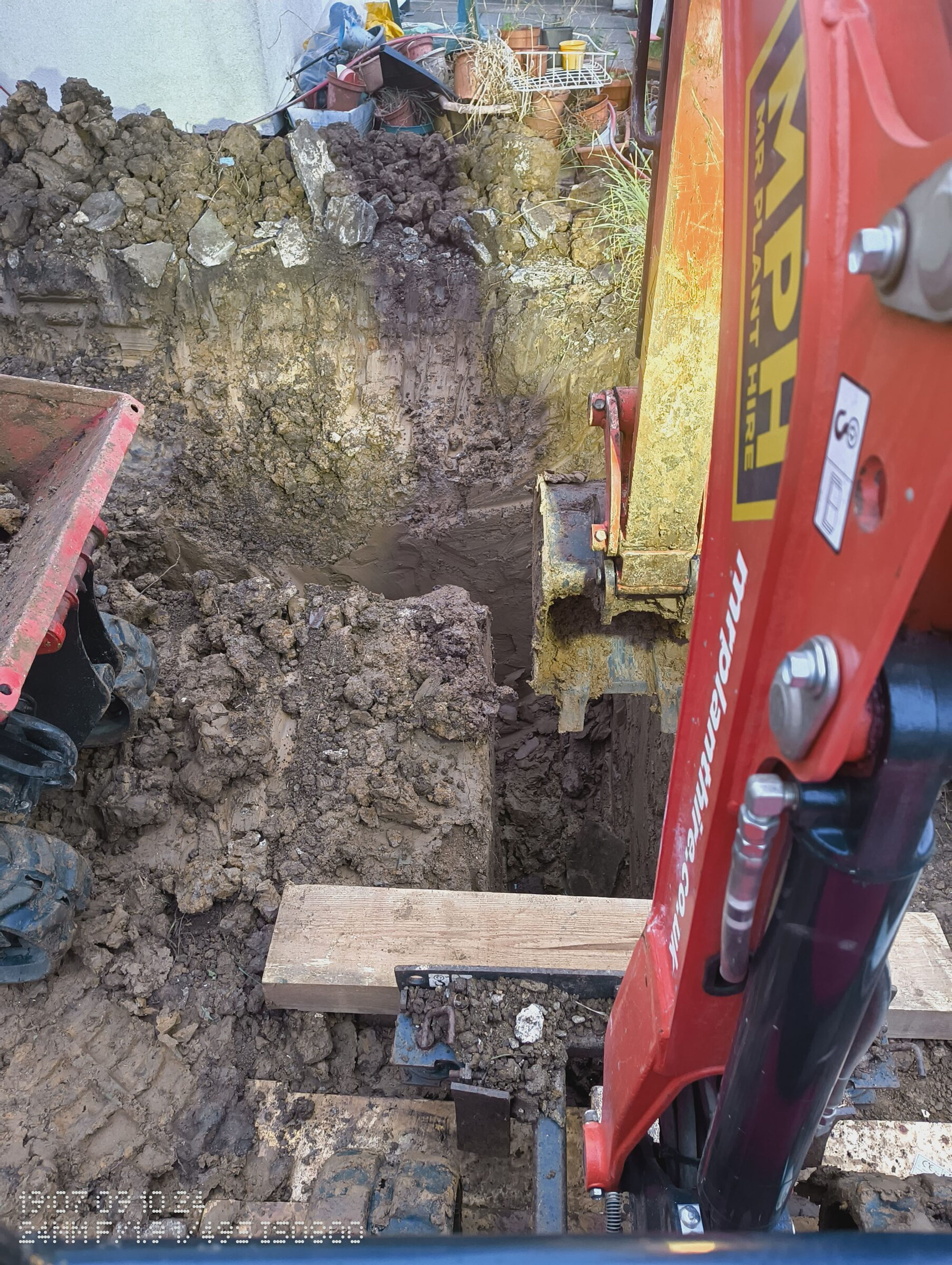 Mini digger working in a deep foundation trench beside a spoil heap on a Chigwell rear extension.