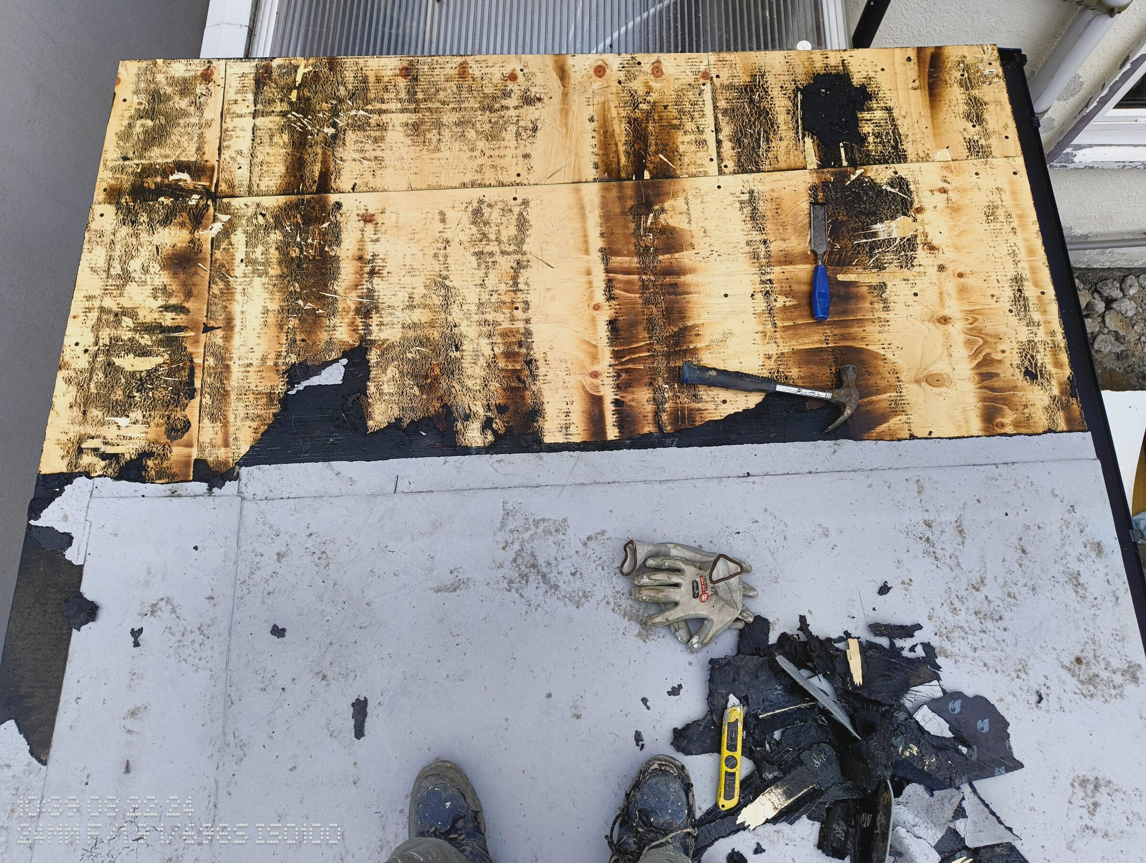 Timber roof deck exposed after the felt was stripped, with a hammer, chisel, and cut felt on the roof.