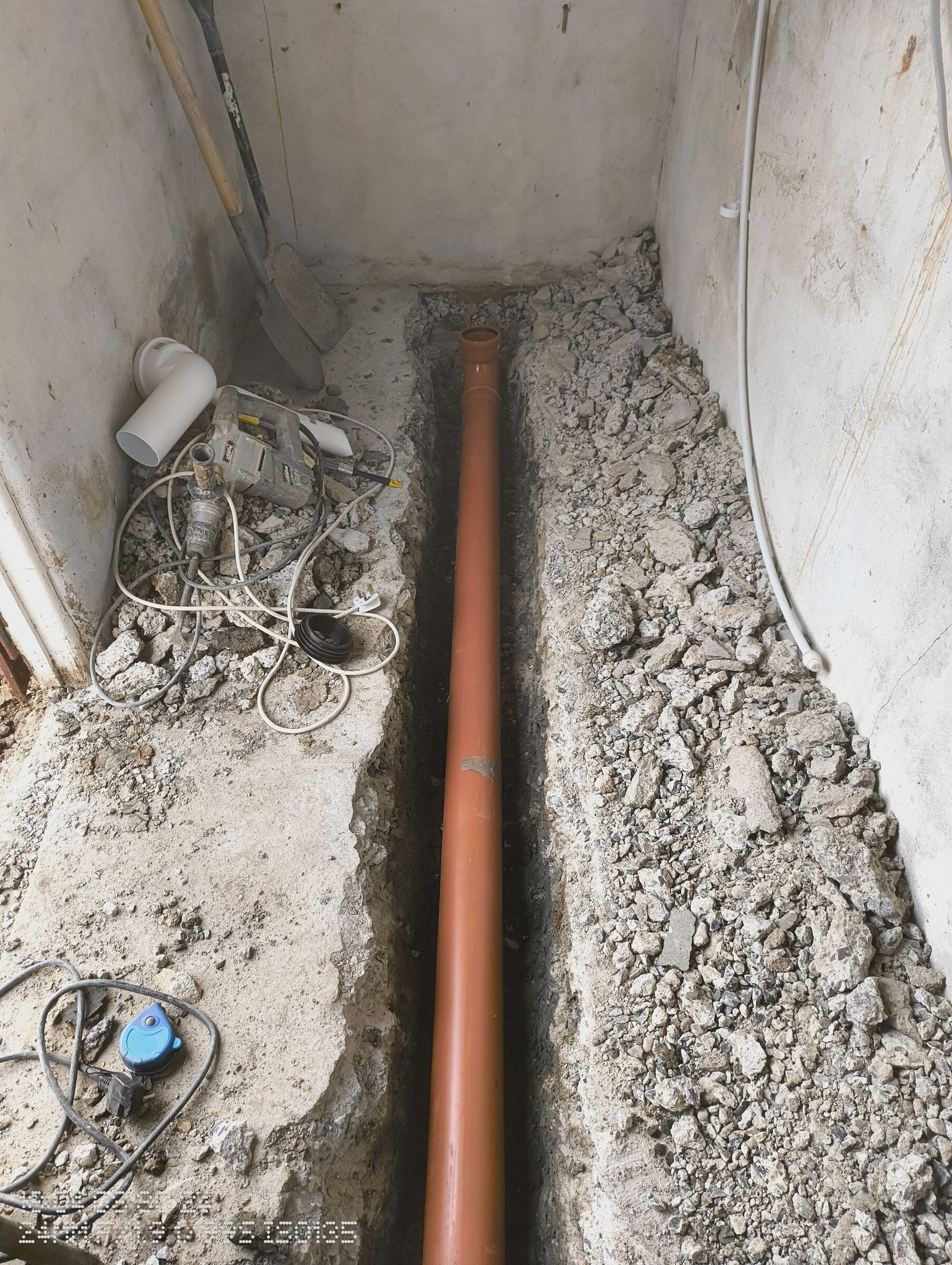 New orange drainage pipe laid in the channel cut through the internal concrete floor.