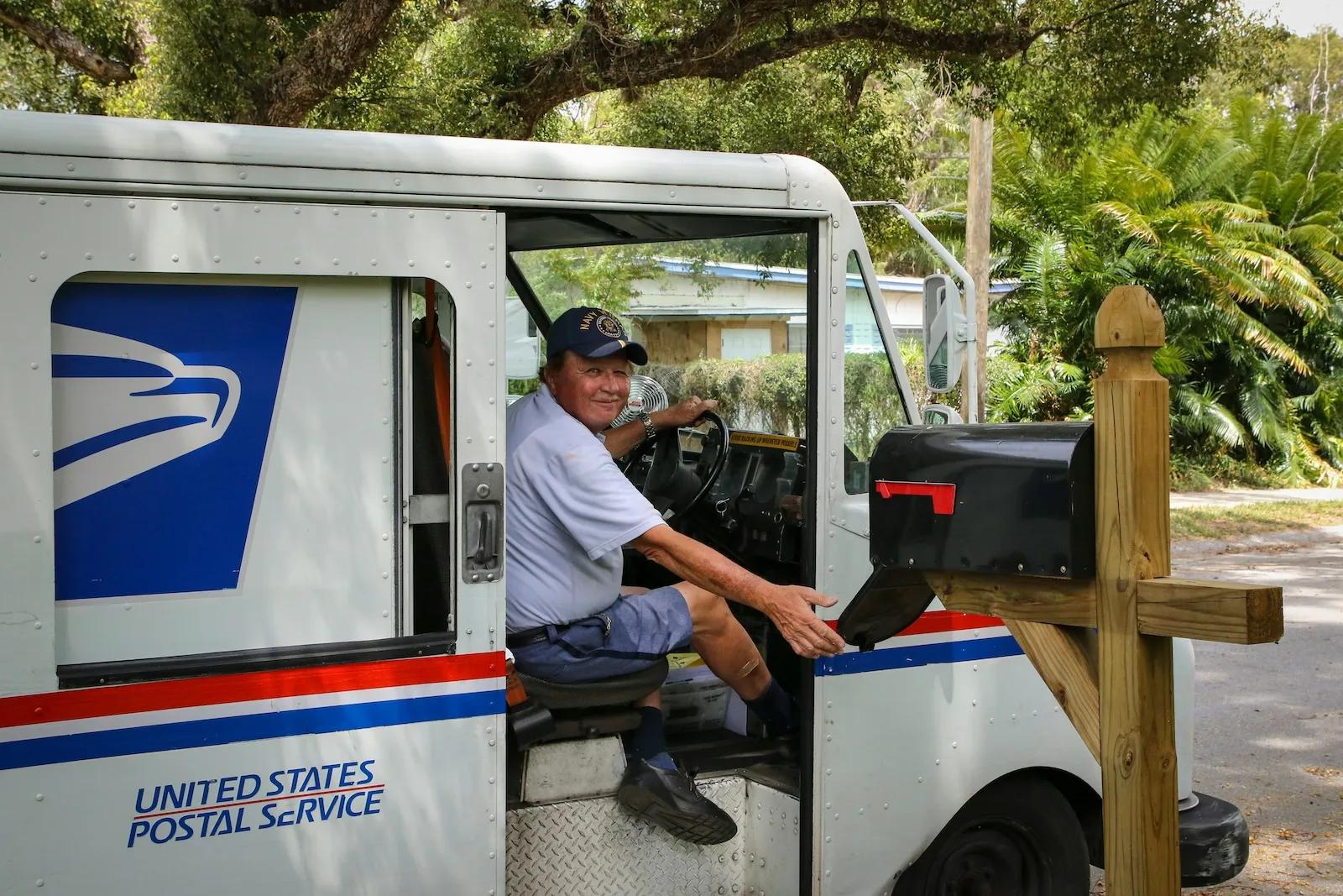 USPS mail carrier delivering mail to mailbox, representing mail handling and forwarding services