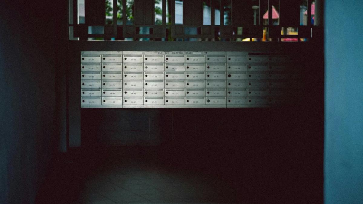 Wall of numbered mailboxes in a dim apartment corridor, representing the traditional mailroom setup businesses are replacing with mail forwarding services