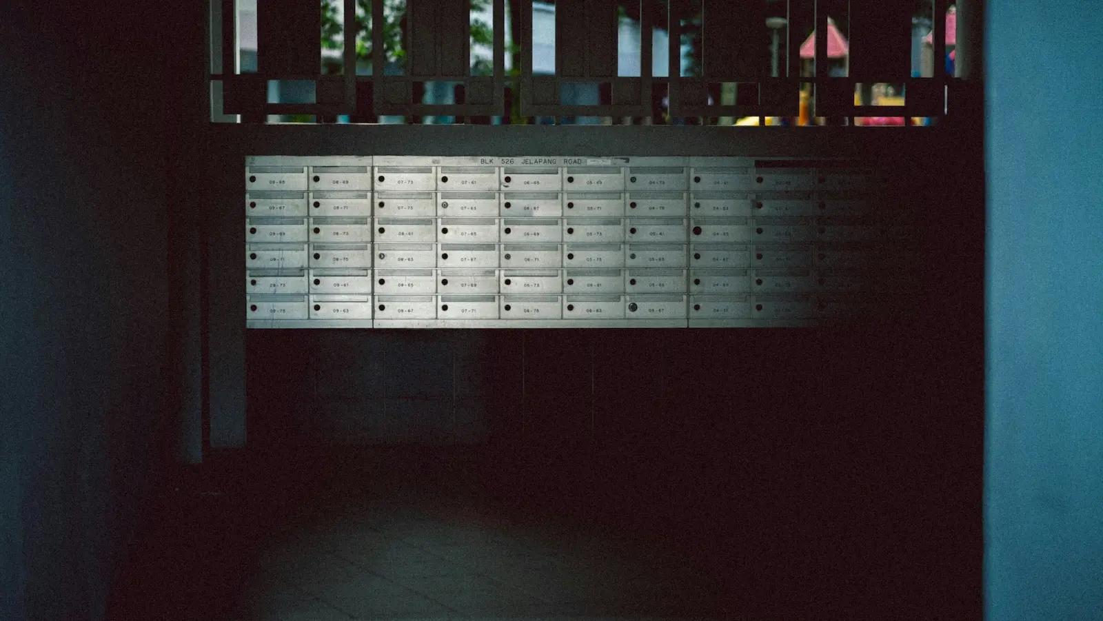 Wall of numbered mailboxes in a dim apartment corridor, representing the traditional mailroom setup businesses are replacing with mail forwarding services