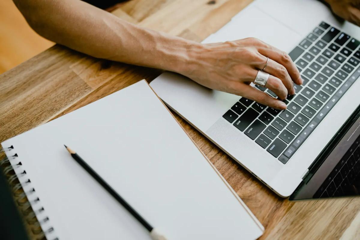 Person working on a laptop beside a notebook, representing the shift from manual to digital mail management