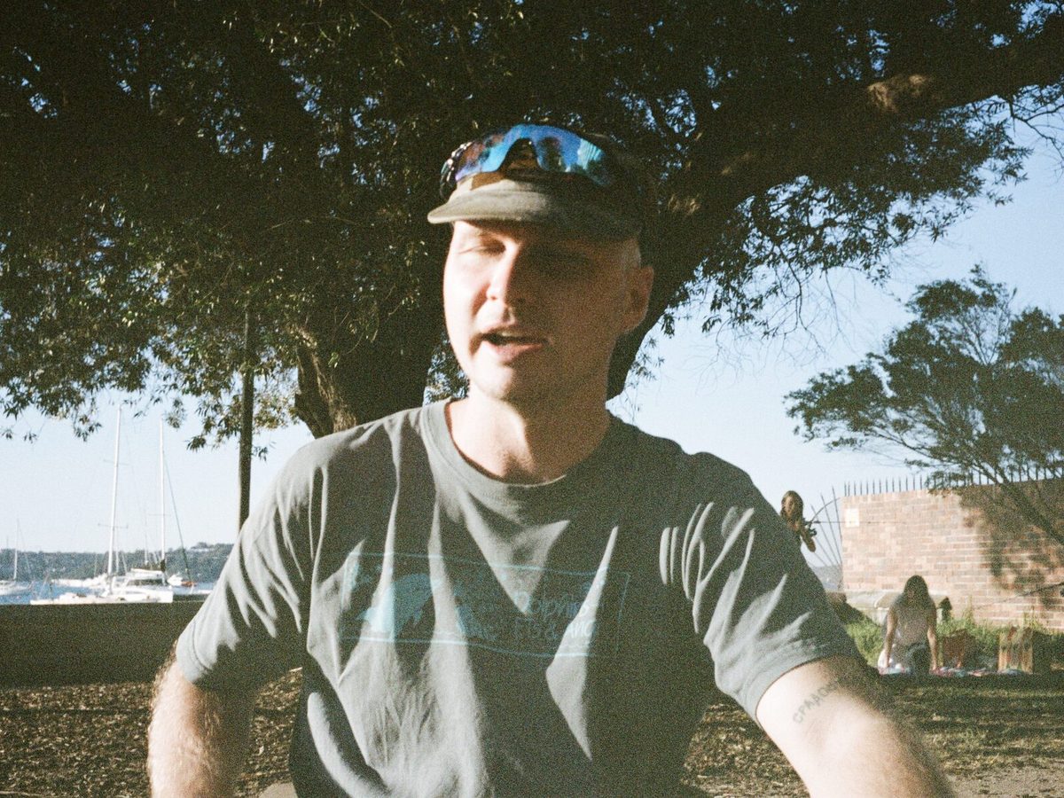 Sam, founder and director of Soul Support, on the Gold Coast. He sits outside, reaching toward something, with his mouth open as if he's mid conversation. On his head, he wears a hat. His sunglasses are resting on his hat. The sun shines on his face, and his eyes are closed. This may be because he's looking into the sun and not wearing his sunglasses on his eyes, or because it's impossible to find a photo of him when he's not blinking.