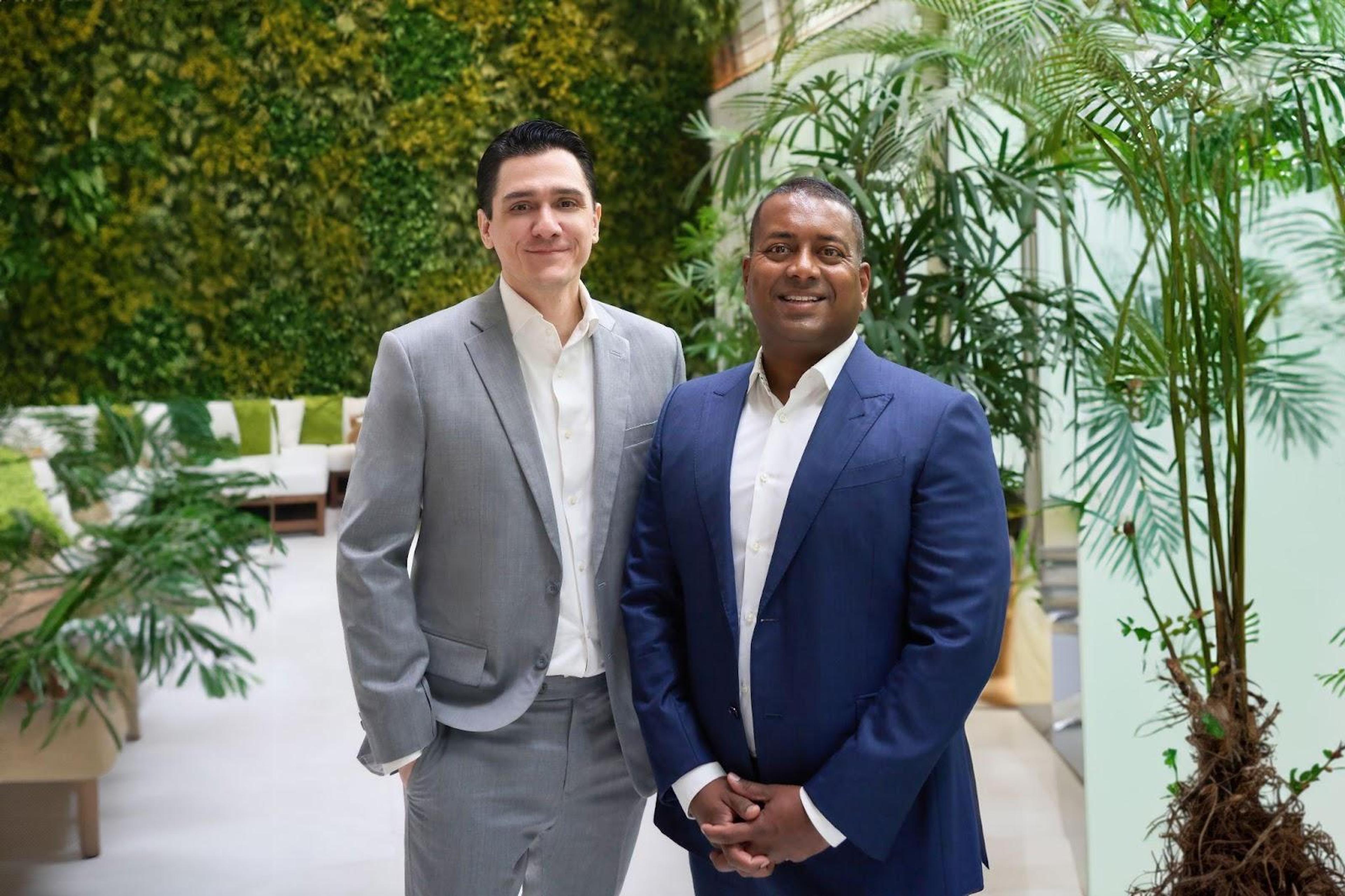 Two men standing together in front of plantsDescription automatically generated