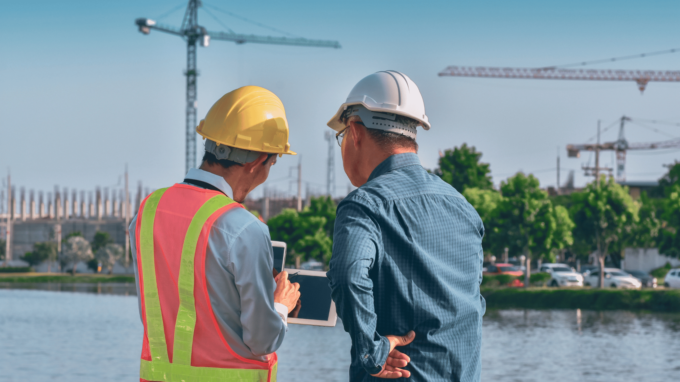 Two construction professionals reviewing a tablet near tower cranes