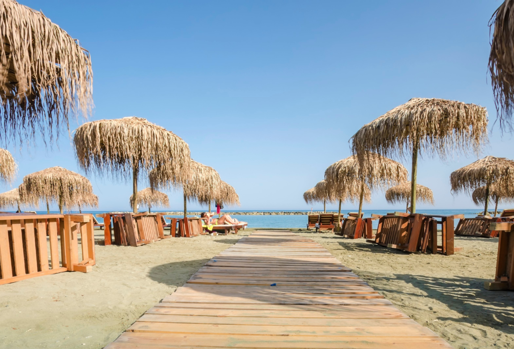 Träbrygga mellan solparasoll som leder ner till havet