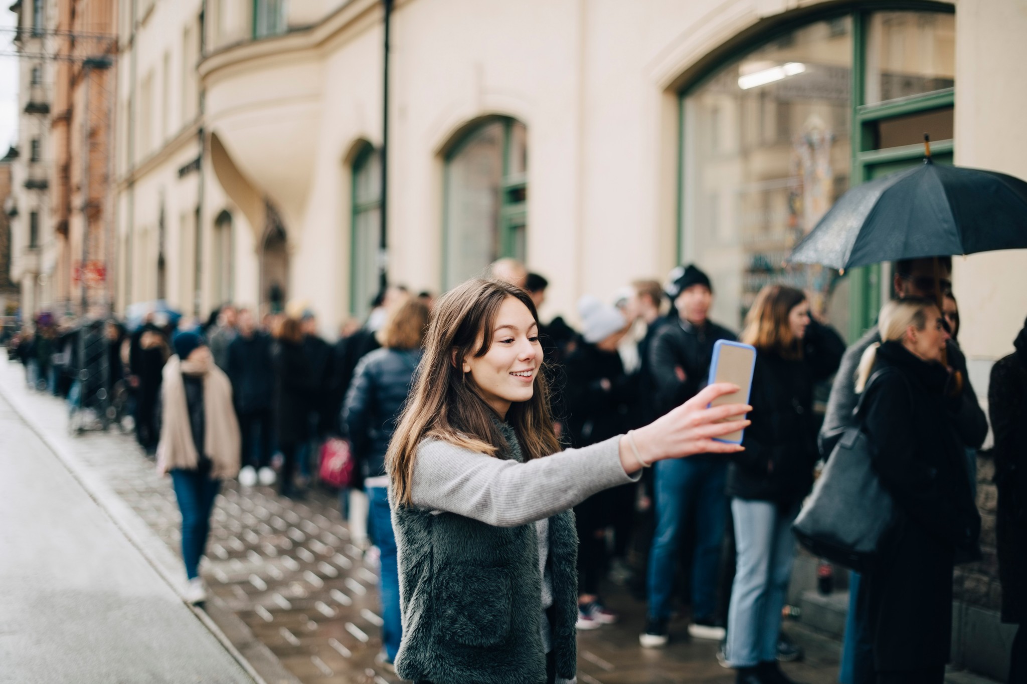 Kvinna som går förbi en kö och tittar på sin telefon