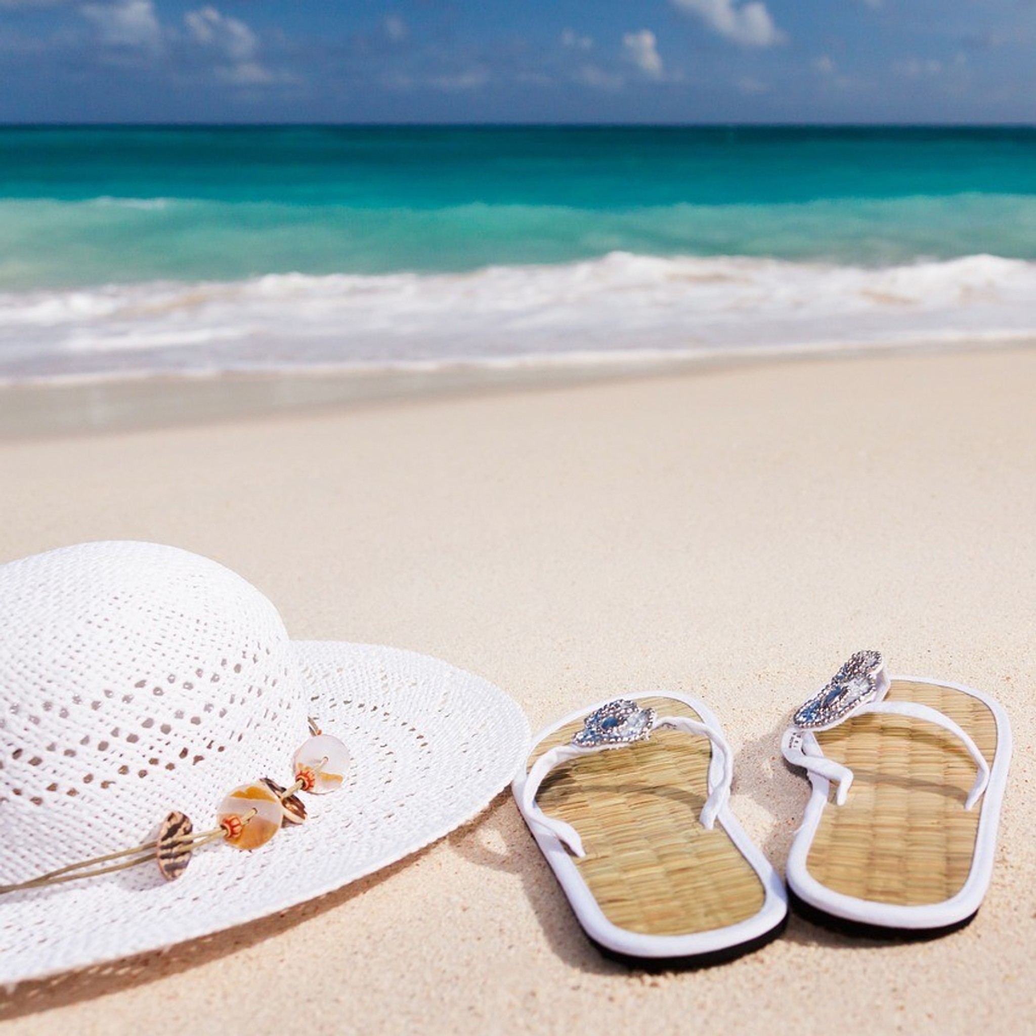 Solhatt och sandaler på en vit strand