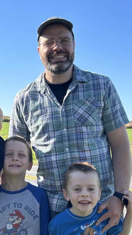 Shane Linetty smiling outdoors in a cap and plaid shirt with his children.