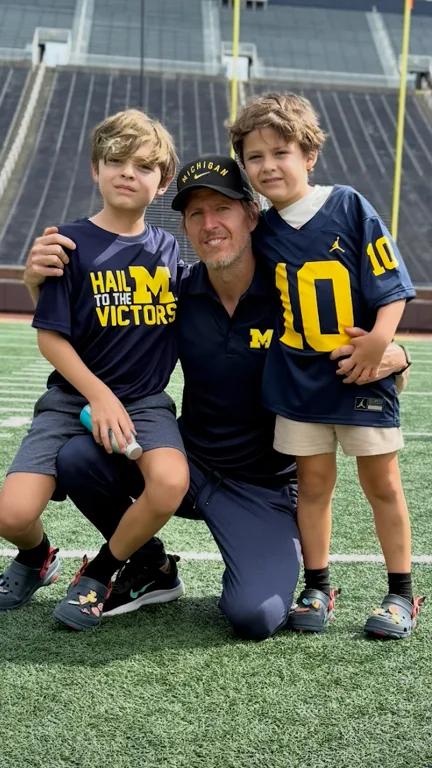 Dony West smiling with his two children on the field at Michigan Stadium.