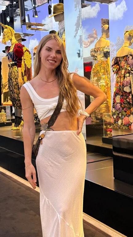 Ana Washington smiling in a white dress beside a mirrored fashion display.