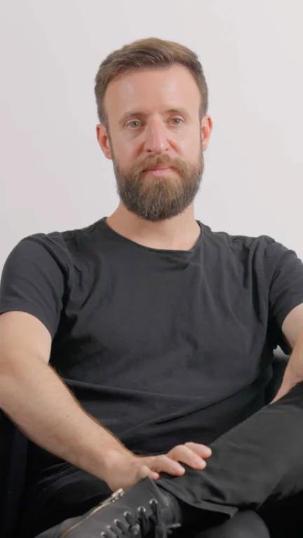 Jonathan seated with one leg crossed, wearing a dark T-shirt against a light background.