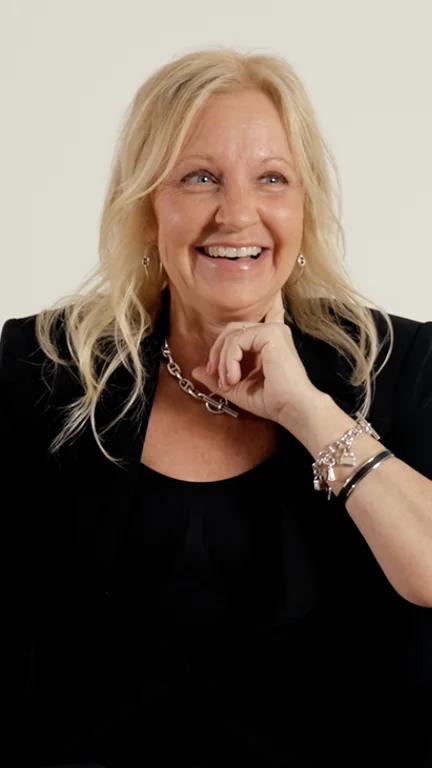 Cari smiling in a black outfit, seated against a light background.