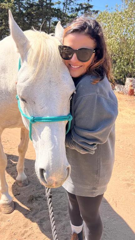 Melissa Zeidler smiling in sunglasses beside a white horse outdoors.