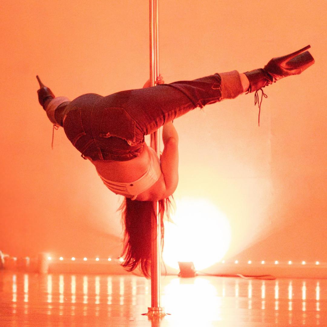 A dancer inverted on the pole in warm light