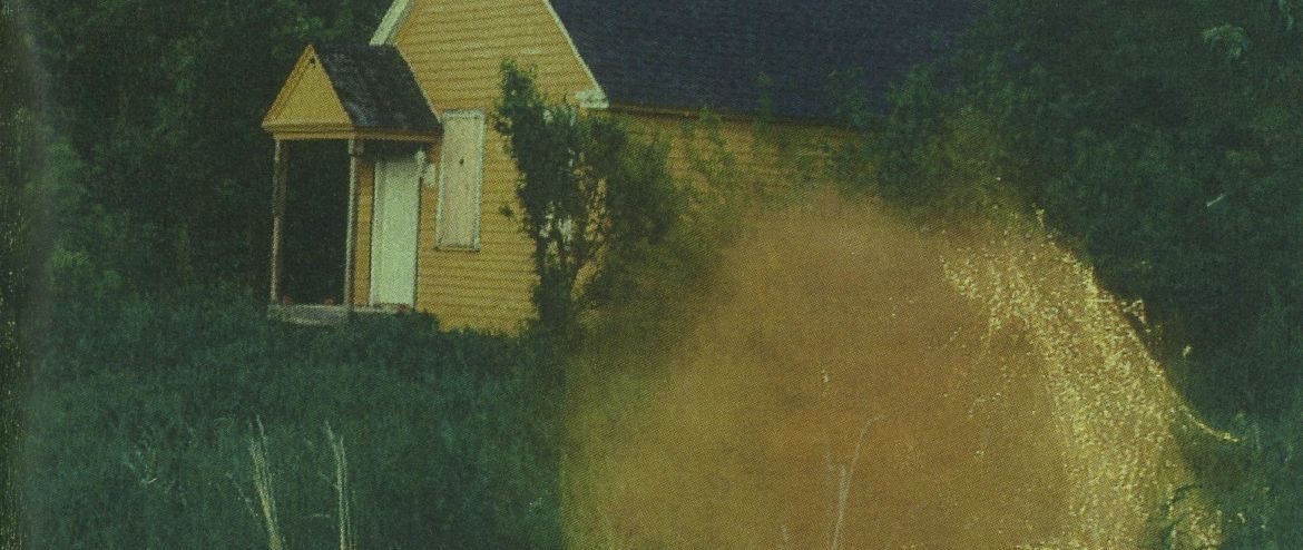 An open book showing a page of text and credits on the left, and a photograph on the right of a yellow house in tall grass with an orange light flare.