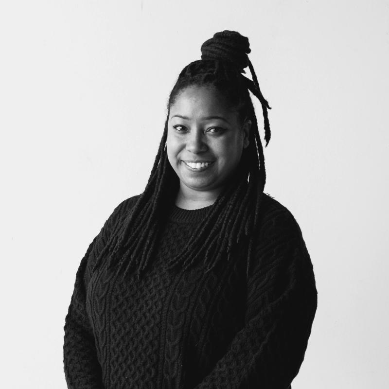 Black and white photo of a smiling woman with dreadlocks and a dark sweater.