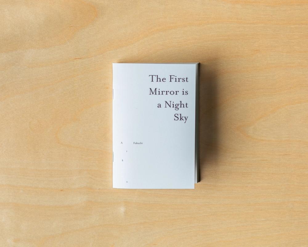 a book titled the first mirror is a night sky is sitting on a wooden table .