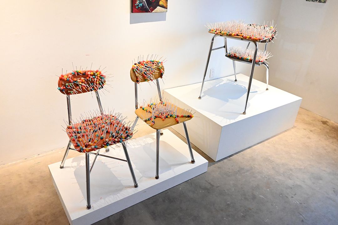 Art installation of chairs and a desk covered in colorful candies with numerous pointed sticks protruding.