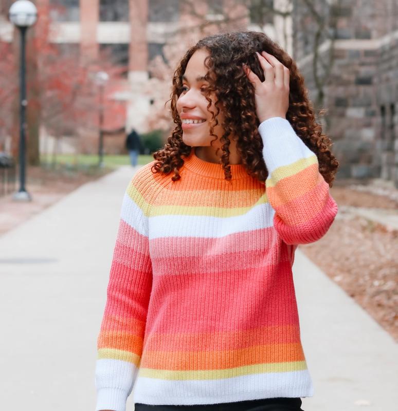 a girl with curly hair wearing a rainbow striped sweater