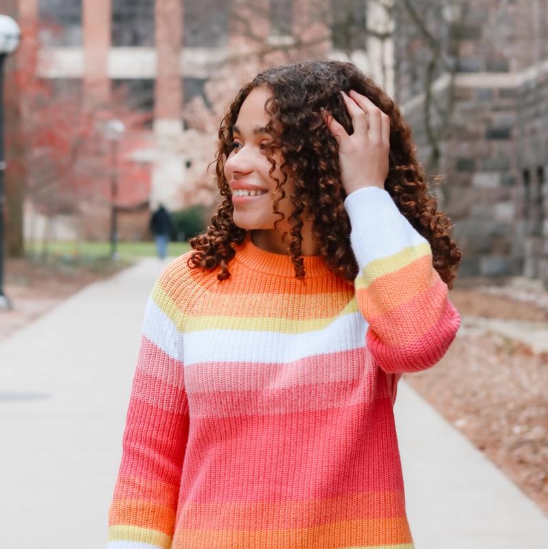 a girl with curly hair wearing a rainbow striped sweater