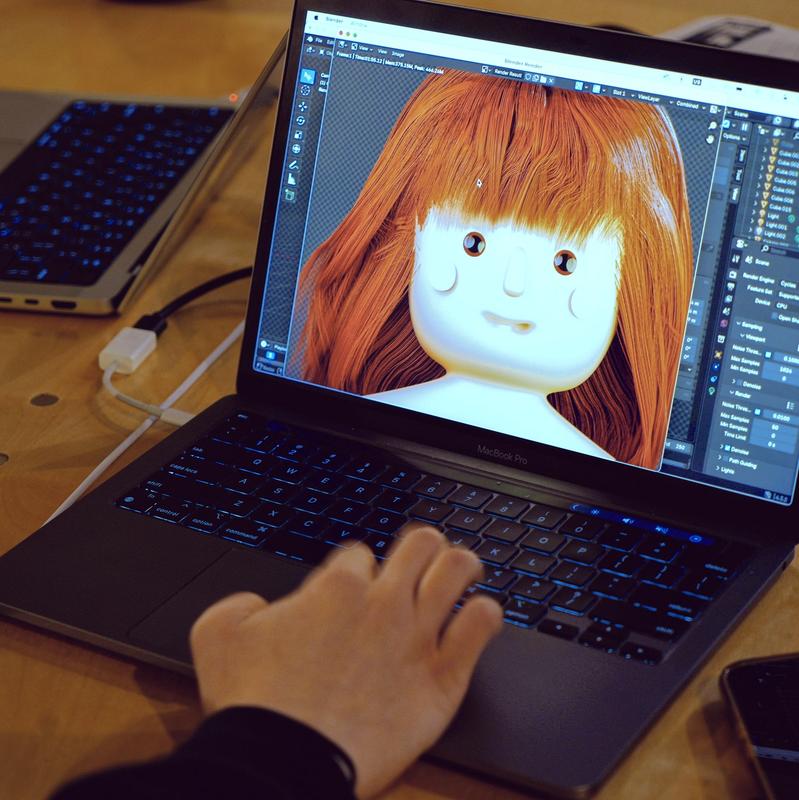 a person is typing on a laptop computer with a doll on the screen .