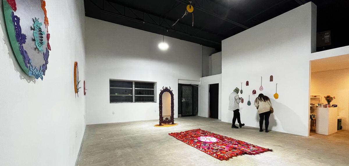 Two visitors observe colorful, varied artworks in a spacious modern gallery with white walls and a concrete floor.