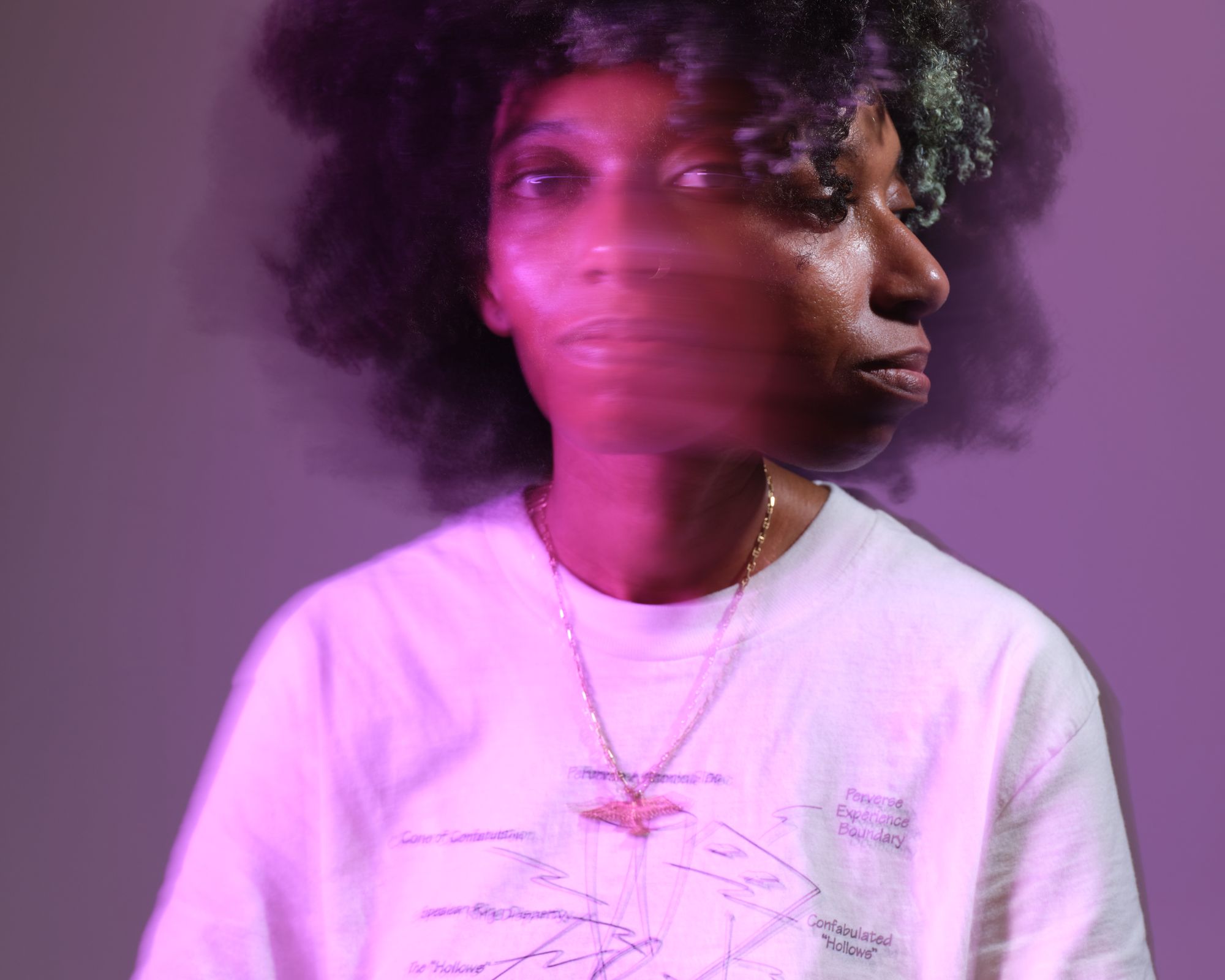 a woman with curly hair is wearing a white t-shirt and a necklace .