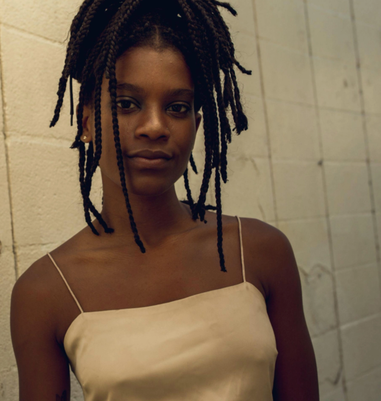 a woman with dreadlocks is wearing a tan tank top