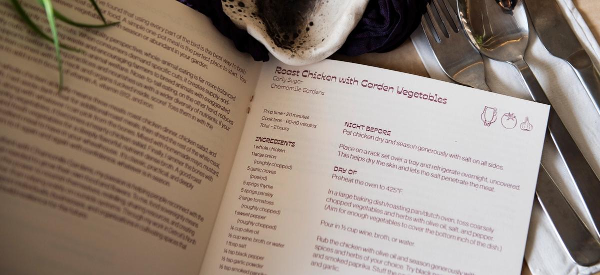 An open cookbook showing a "Roast Chicken with Garden Vegetables" recipe, with a fork, spoon, and knife beside it.