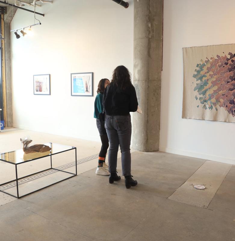 two women are standing in a room looking at a painting .
