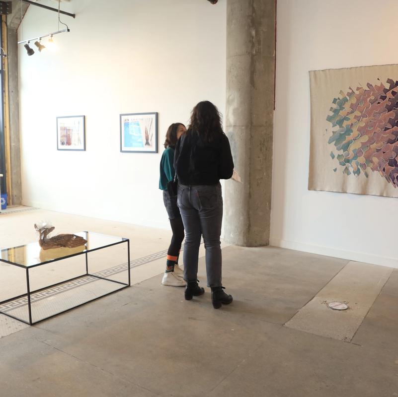 two women are standing in a room looking at a painting .