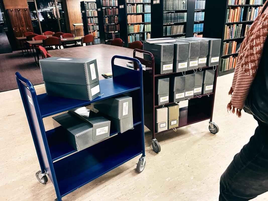 a person is standing next to a cart filled with boxes in a library .