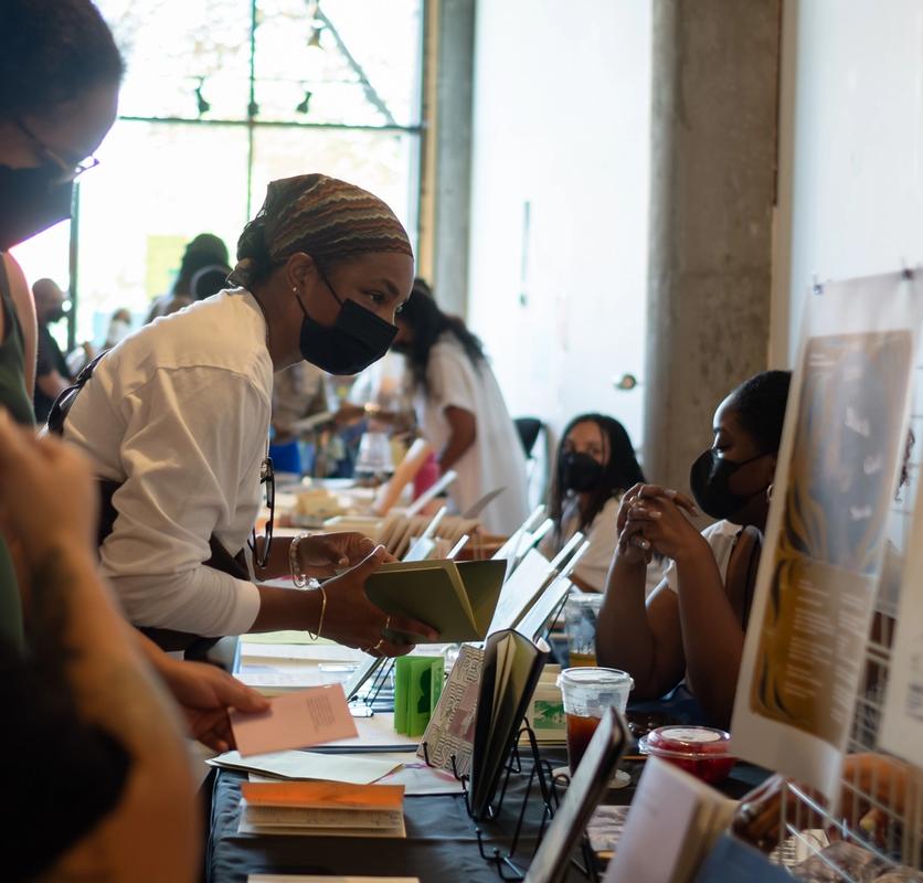 a woman wearing a mask is standing at a table with other people .