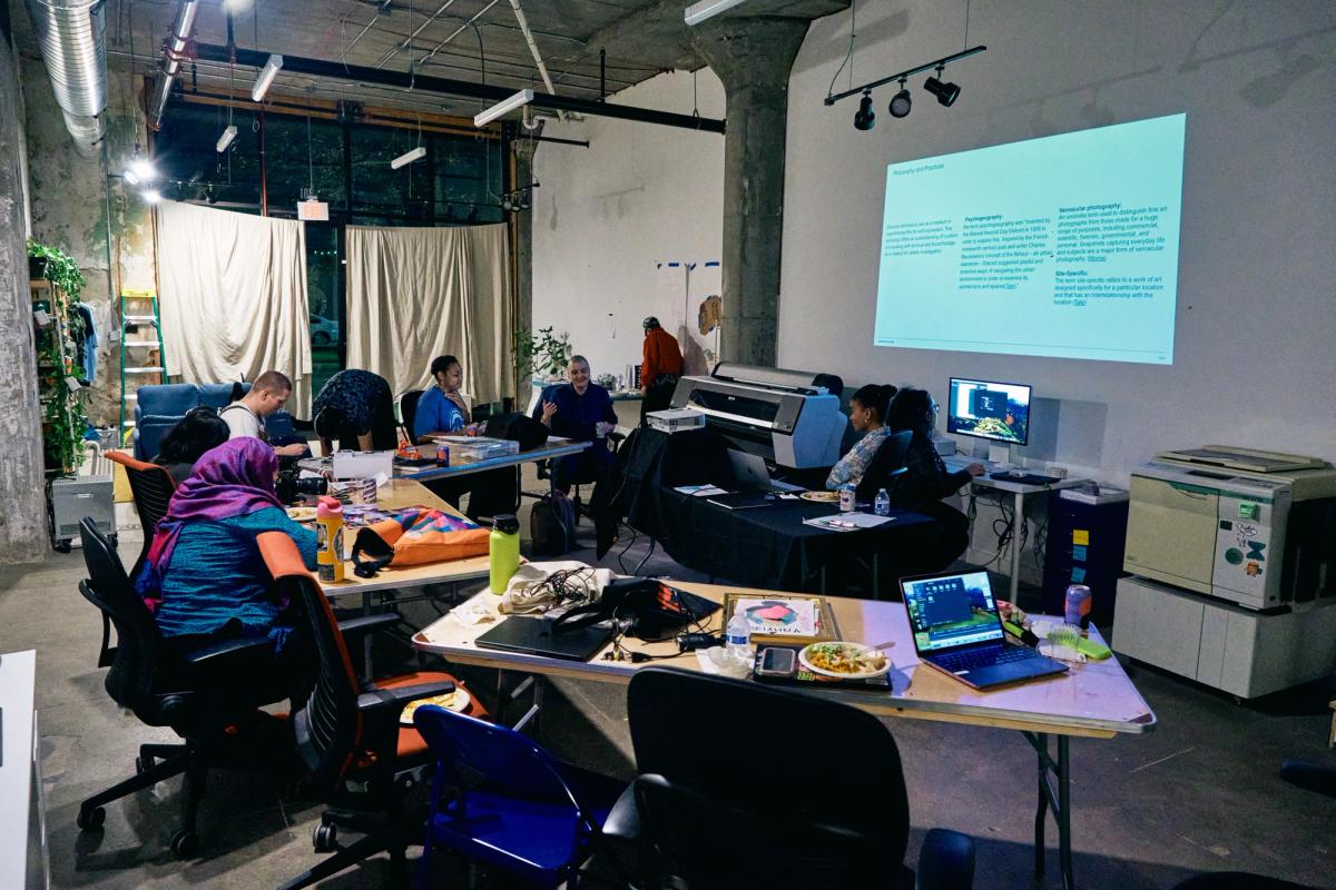 a group of people are sitting at tables in a room with a projector screen .