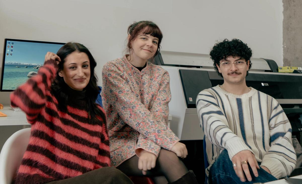 Three smiling people sit in a bright office with "GD 101 WE'RE GLAD YOU'RE HERE" projected on the wall.