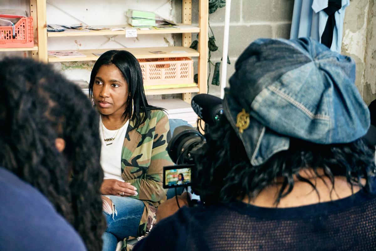 a woman is sitting in front of a camera talking to another woman .
