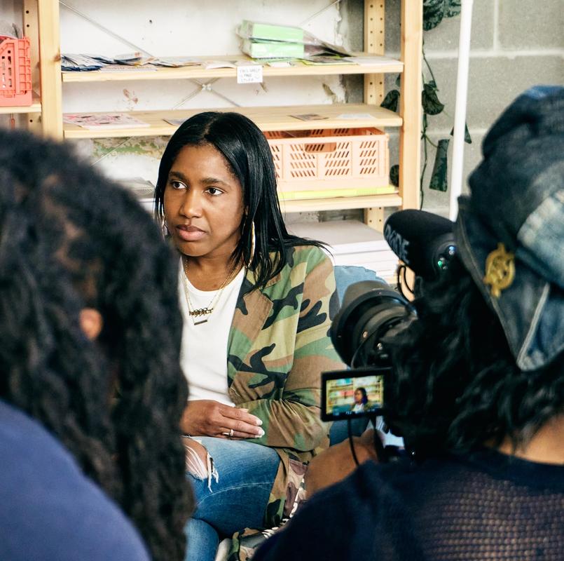a woman is sitting in front of a camera talking to another woman .