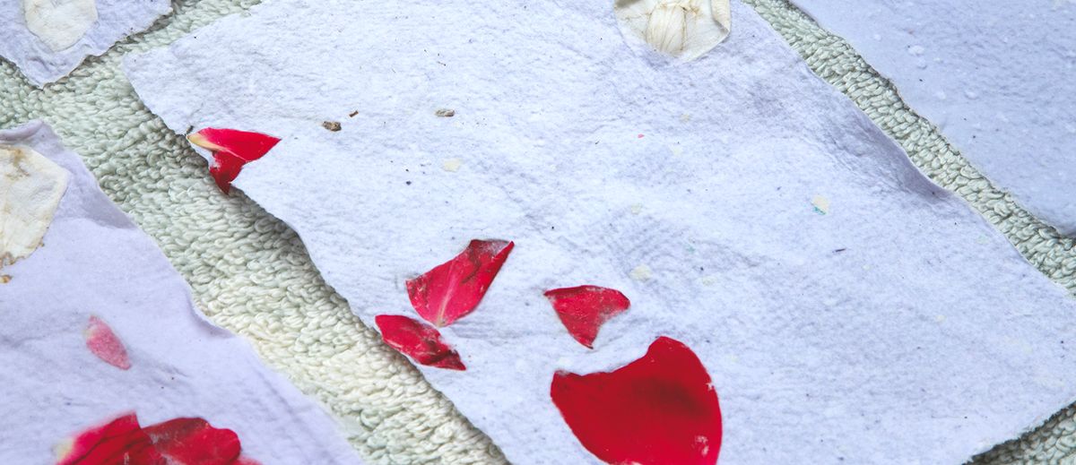 Handmade light blue and white paper with red flower petals drying on a green towel.