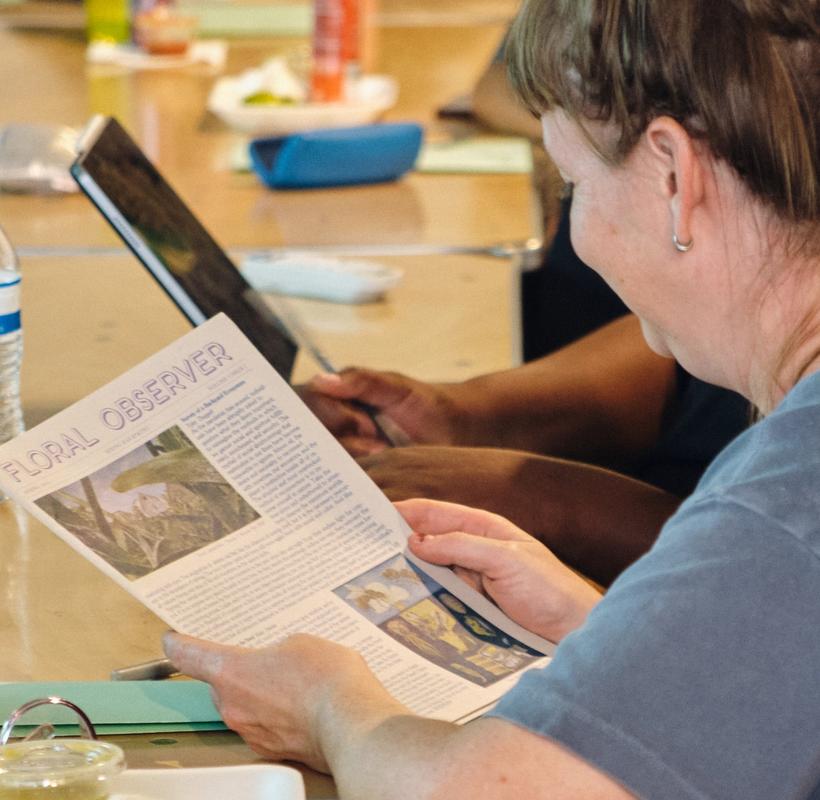 a group of people are sitting at a table reading a newspaper .