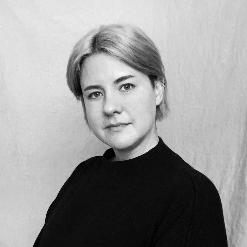Black and white headshot of a woman with short light hair and a nose ring, wearing a dark top.