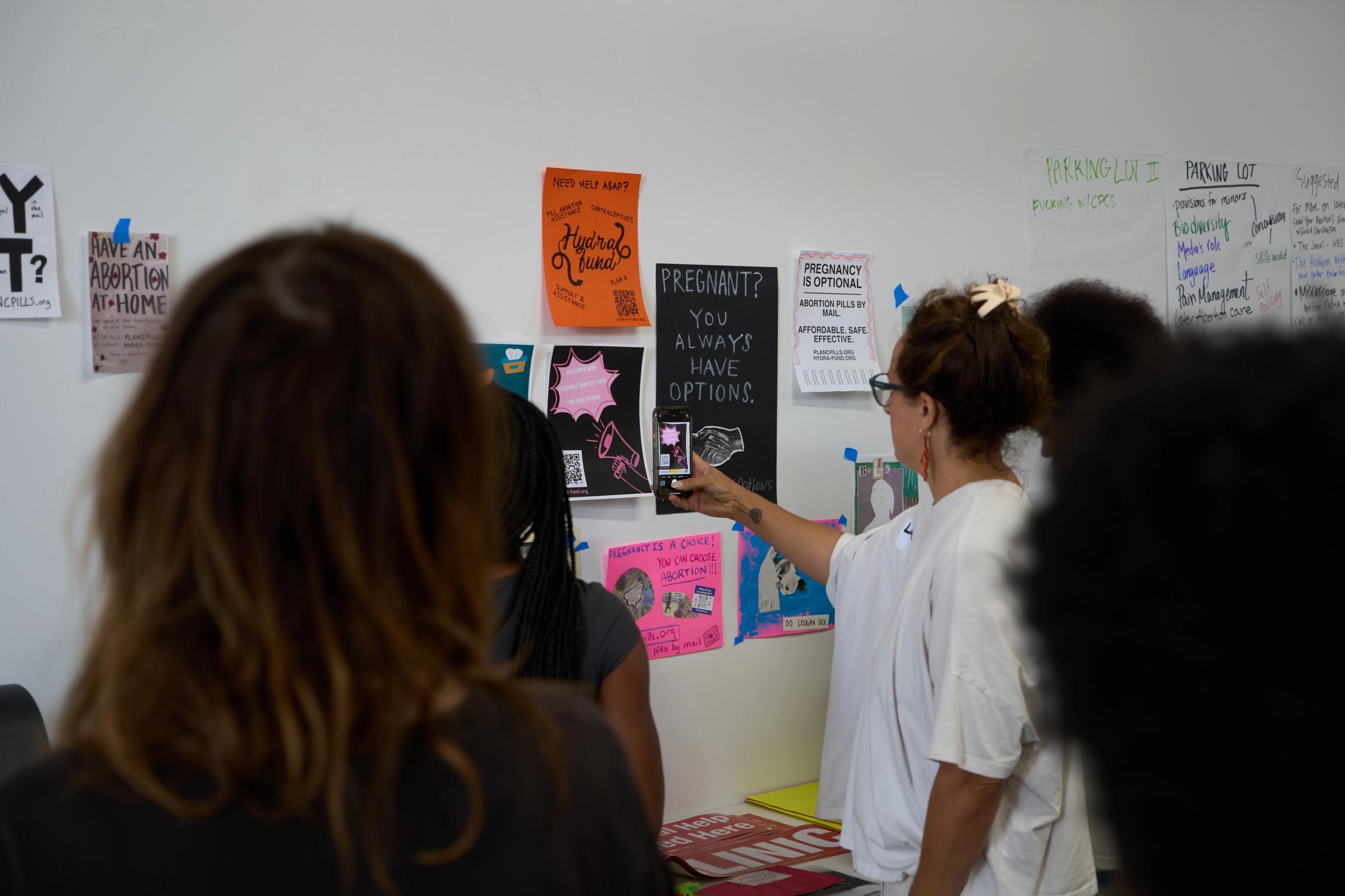 a group of women are standing in front of a wall with posters on it .
