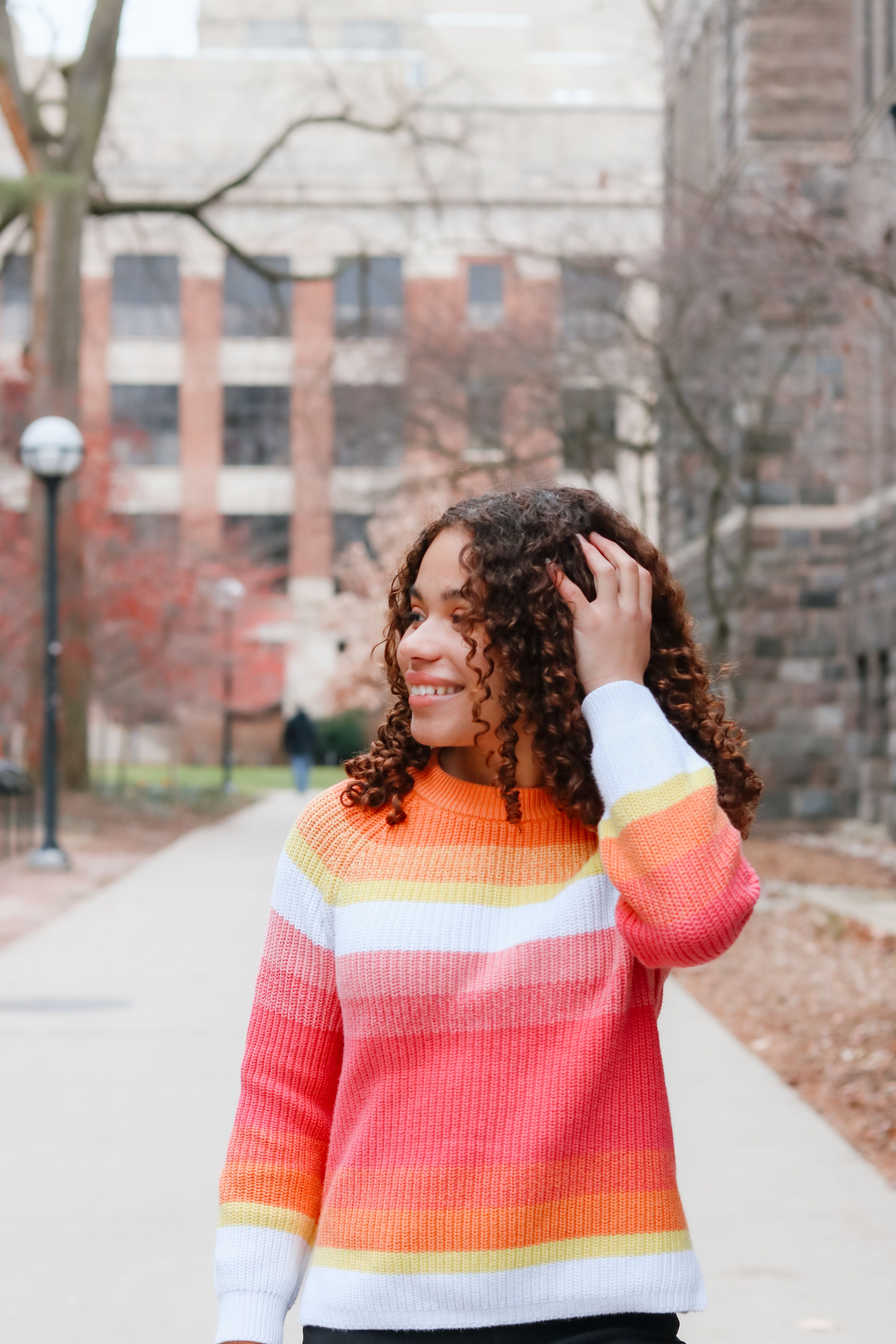 a girl with curly hair wearing a rainbow striped sweater