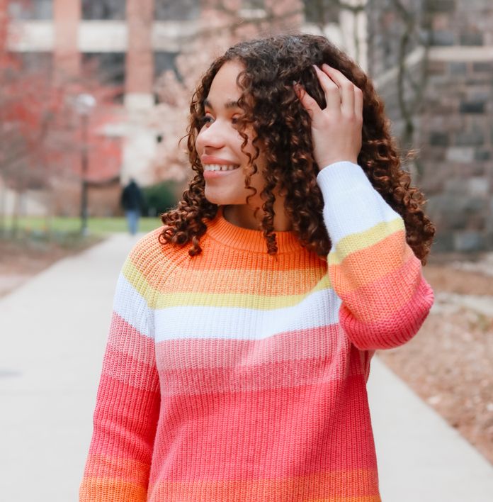 a girl with curly hair wearing a rainbow striped sweater
