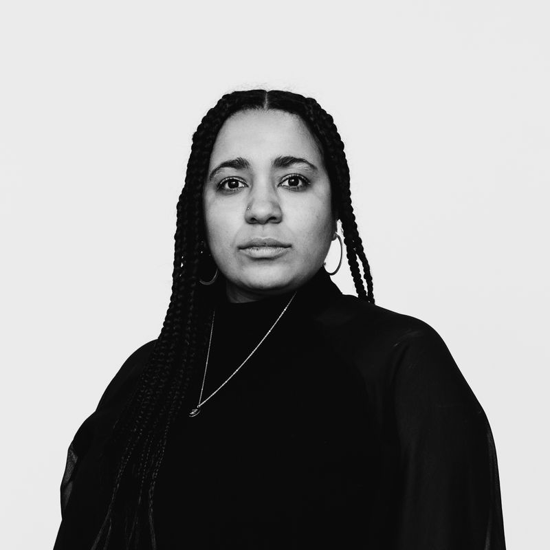 Black and white portrait of a woman with long braids, wearing a dark top and necklace.